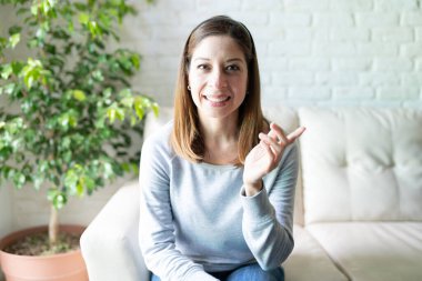 40 'lı yaşlarda tatlı bir kadının oturma odasında oturmuş, bir video görüşmesi sırasında konuştuğu portre.