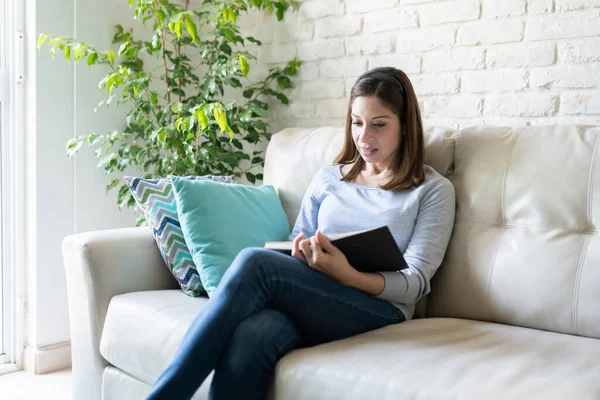 Mulher Morena Atraente Sentada Sofá Desfrutando Bom Livro Enquanto Relaxa — Fotografia de Stock