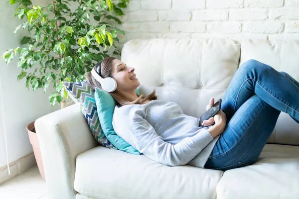 ソファに横たわりながらヘッドフォンをしている女性のプロフィールビューと自宅で彼女の好きな音楽とリラックス — ストック写真