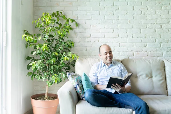 Good looking bald man relaxing at home and enjoying a good book while sitting in a couch. Plenty of copy space