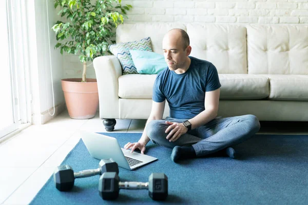 白种人秃头的男人在笔记本电脑上找一些在线锻炼 准备在家里锻炼和锻炼 — 图库照片