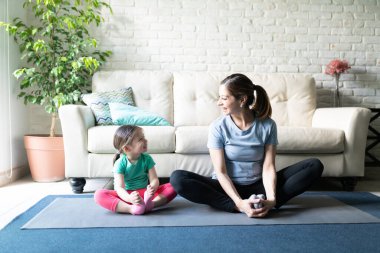 Güzel bir kadın ve kızının bir yoga minderinde esneyip egzersiz yaptığı ve birbirlerine gülümseyen portresi.