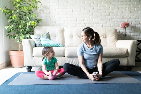 一个漂亮的女人和她的女儿在瑜伽垫上一起伸展和锻炼 面带微笑地看着对方的画像 — 图库照片