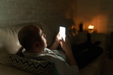 30 'lu yaşlarda bir adamın gece evde bir kanepede yatarken kız arkadaşına mesaj atması.