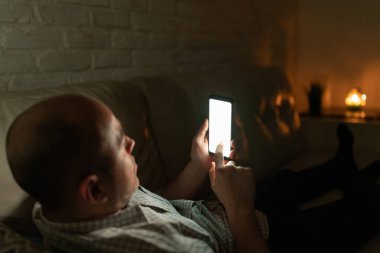 Kel bir adamın gece yarısı beyaz bir akıllı telefona dokunuşunun görüntüsü. Ekrana odaklan.