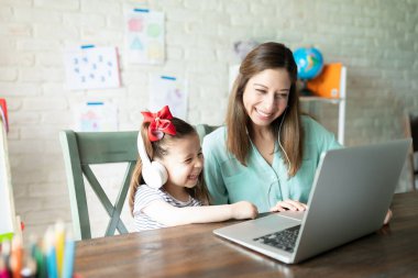 Anne ve kızı evde dizüstü bilgisayarda eğlenceli bir dizi izliyor ve birlikte gülüyorlar.