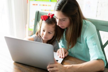 Beyaz anne ve kızı evde eğitim ve öğretim için dizüstü bilgisayar kullanıyor.