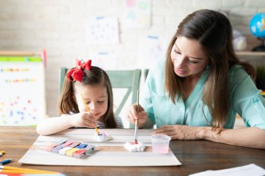 Güzel anne ve kız suluboya kullanıyor ve evde okul yaparken alçı figürler çiziyorlar.