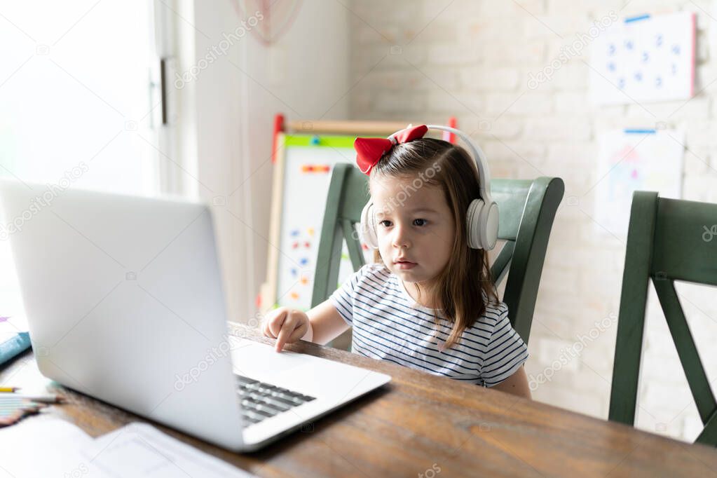 Adorable little girl using a laptop computer and headphones for learning online at home