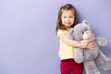 Küçük sevimli bir kızın portresi oyuncak ayıya sarılıyor ve bir stüdyoda fotokopi odası ile gülümsüyor.