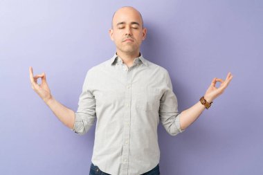 Rahat giyinen ve bir stüdyoda gözleri kapalı meditasyon yapan bir adam.