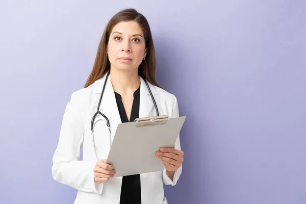 有魅力的女医生拿着病人的档案 在紫色背景的工作室里看起来很严肃 — 图库照片