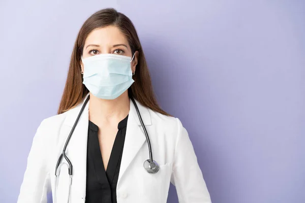 一名女医生戴着面具和实验室外套在紫色背景的工作室中的画像 — 图库照片