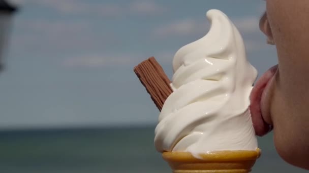 Primer plano de una persona comiendo un cono de helado en un muelle junto al mar — Vídeos de Stock