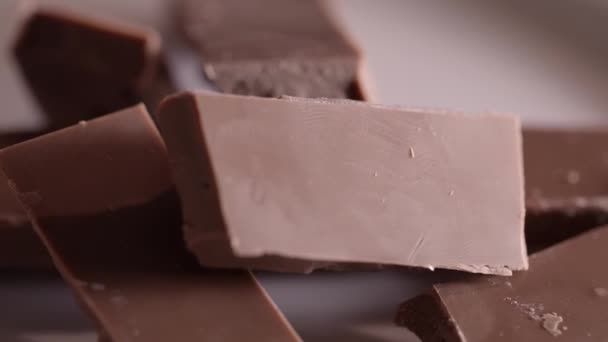 Pedazos de chocolate girando sobre un fondo liso — Vídeo de stock