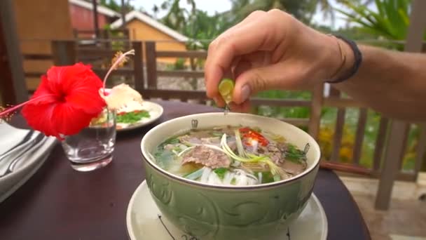 Clipe de câmera lenta de um homem espremendo limão fresco em um ramen macarrão vietnamita — Vídeo de Stock
