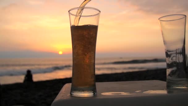 Slow motion shot of beer being poured into a glass on a beach — Stock Video