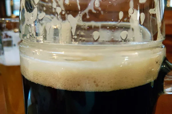 Taza de cerveza oscura con espuma en la mesa, enfoque selectivo . — Foto de Stock