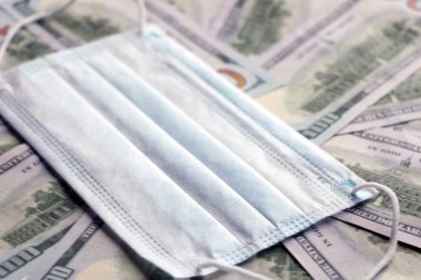 Coronavirüs salgını konsepti. Dolar banknotları üzerinde tıbbi koruyucu maske. Kopyalama için bir yer var.