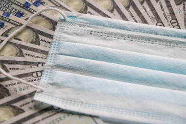 Coronavirüs salgını konsepti. Dolar banknotları üzerinde tıbbi koruyucu maske. Kopyalama için bir yer var.