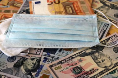 Solunum yollarının virüsten korunmasının bir sembolü olarak dolar ve avroya uygulanan tıbbi maske. Kopyalama için bir yer var.