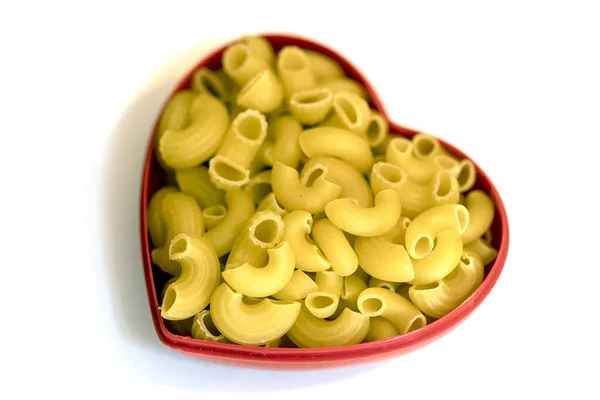 Pasta italiana curva all'interno di un contenitore a forma di cuore, isolata su fondo bianco . — Foto Stock