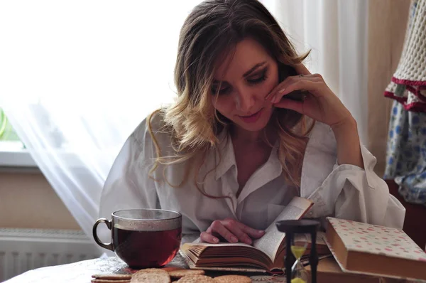 Genç güzel kadın tarafından ahşap masa oturma ve kitap okuma