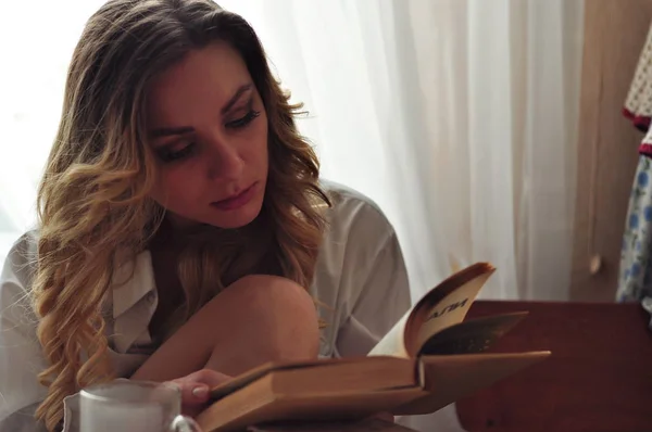 Genç güzel kadın tarafından ahşap masa oturma ve kitap okuma