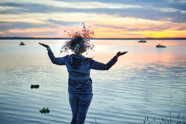 Gölün kıyısında kır çiçeklerinden bir çelenk taşıyan bir kadın. Göl kenarındaki Aziz John arifesinde bir akşam. Litvanya 'da yaz ortası halk festivali