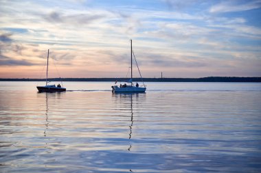 Gölün kıyısında kır çiçeklerinden bir çelenk taşıyan bir kadın. Göl kenarındaki Aziz John arifesinde bir akşam. Litvanya 'da yaz ortası halk festivali