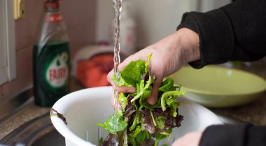 Kadın eli lavabonun altında marul yıkıyor.