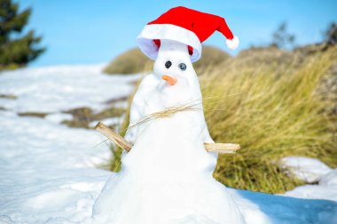 Mavi gökyüzü arka planında Noel şapkalı bir kardan adam..