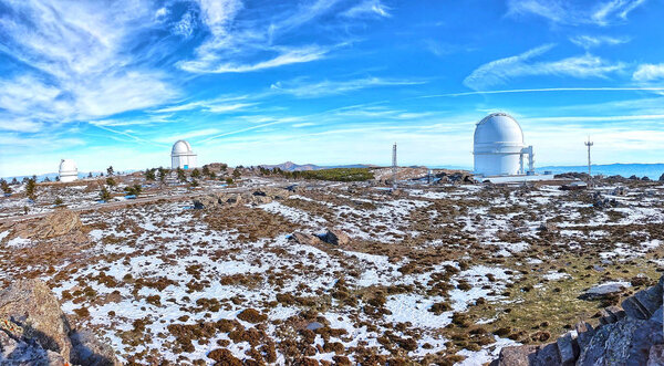 Panoramic of Calar Alto Observatory at the snowy mountain top in Almeria, Andalusia, Spain, 2019. Sky passing through against the domes.