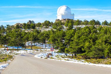 Road to Calar Alto Observatory at the snowy mountain top in Almeria, Andalusia, Spain, 2019. Sky passing through against the domes. clipart