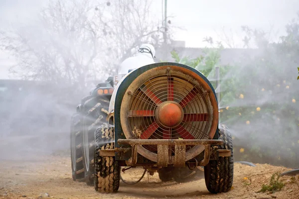 Задній вид трактора розпилює пестициди і інсектициди на лимонних плантаціях в Іспанії. Споживання м'яса інсектицидами. Органічне екологічне сільське господарство. Машина розпилювача, переслідувана трактором гербіцидом. — стокове фото