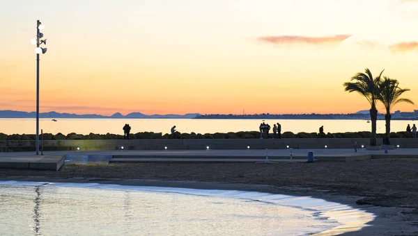 Παραλία Torrevieja κατά την ανατολή του ηλίου. Οι άνθρωποι που περπατούν σε εξωτερικούς χώρους απολαμβάνουν τη θέα. — Φωτογραφία Αρχείου