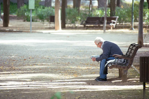 Albacete, spanien, 18. januar 2020: ein älterer herr sitzt auf einer hölzernen bank und liest eine zeitung im abelardo sanchez park. — Stockfoto