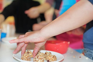 Çocukların elleri yulaf, kuru üzüm, badem ve baldan toplar yapıyor. Çocuklar tatlı yapar. Çocuklar yemek yapıyor. Kavram. Sağlıklı beslenme alışkanlıkları üzerine yüksek lisans sınıfı..