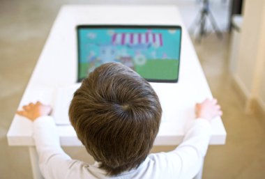 Çocuk tek başına masada bilgisayarını kullanarak ve video izleyerek veya okulda video oyunu oynayarak eğitici bir video izliyor..