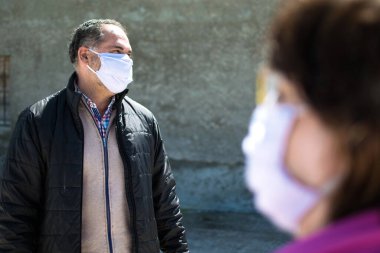 İki kişi güvenlik mesafesini korumaktan, koronavirüs için koruma maskesi takmaktan ya da şehirde covid-19 virüsü salgınından bahsediyor. Corona virüsü, Covid-19, virüs salgını veya sosyal uzaklık kavramı