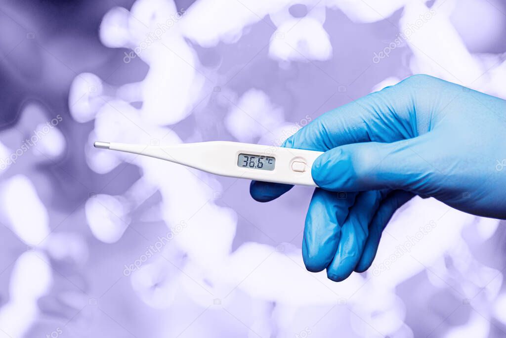 Medical worker in gloves holding an electronic thermometer in his hand against the background of the image of the virus