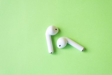 Yeşil arka planda kablosuz beyaz kulaklıklar, mesaj için yer. Renkli bahar konsepti