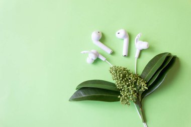 Yeşil arka planda kablosuz beyaz kulaklık. Renkli bahar konsepti. Yaratıcı fikir