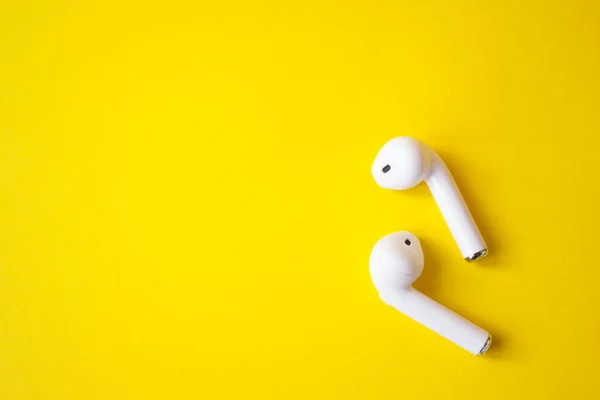 Sarı arka planda kablosuz beyaz kulaklıklar, mesaj için yer. Renkli yaz konsepti