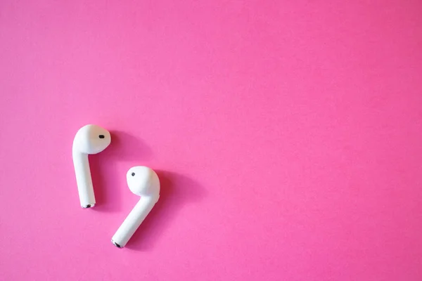 Pembe arka planda kablosuz beyaz kulaklıklar, metin için boşluk