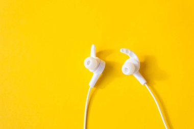 Sarı arka planda dinleme cihazı olan beyaz kulaklıklar. Aygıt kavramı.