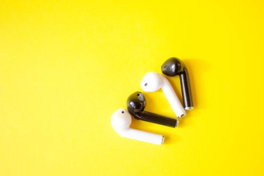 Sarı arka planda kablosuz beyaz ve siyah kulaklıklar. Renkli bahar konsepti. Yaratıcı fikir