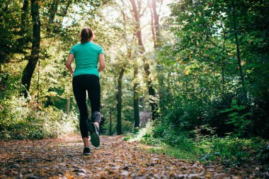 Genç kadın koşuyor yeşil doğaya rağmen