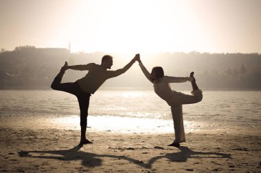 Couple doing dance pose yoga on the beach