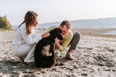 Happy couple spending their leisure time on the beach with the dog